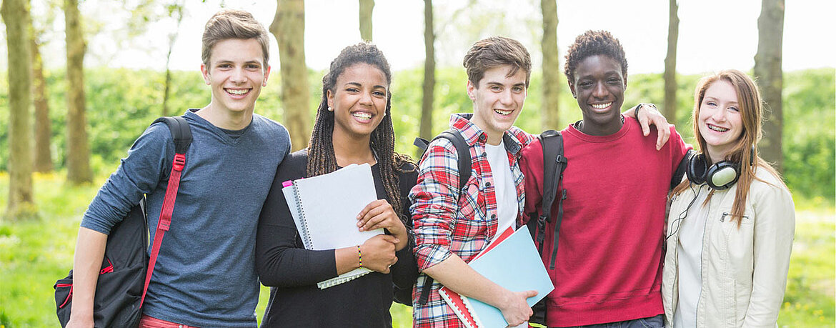 Gruppe von 5 Stundenten in der Natur mit Block und Rucksack